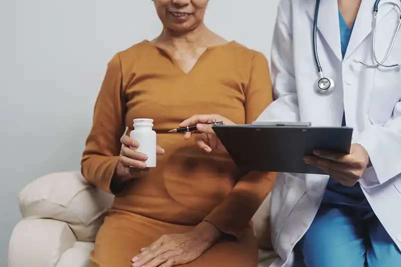 elderly asian female needing chronic care holding pill bottle with doctor