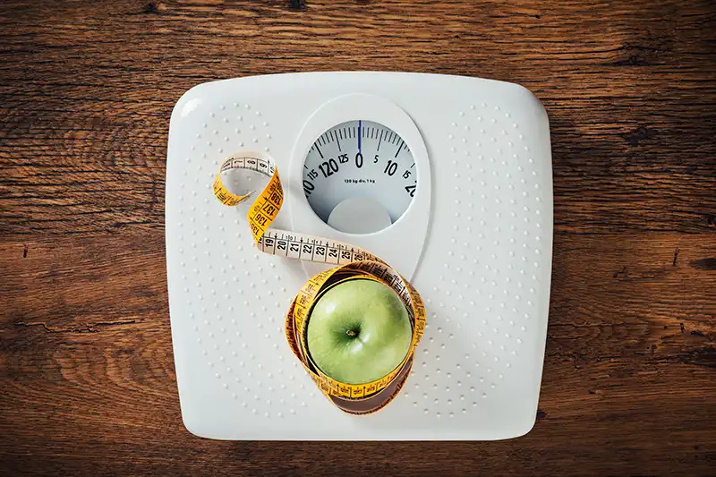 green apple wrapped in measuring tape sitting on weight loss scale