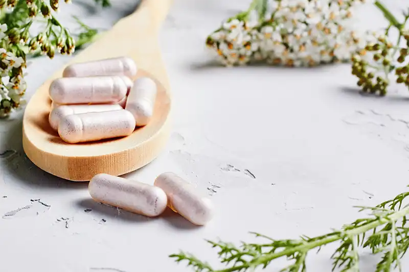 supplement capsules in wooden spoon surrounded by wildflowers