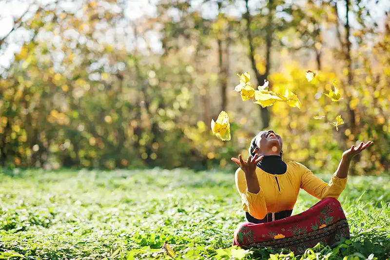young happy black girl sitting in field of yellow flowers