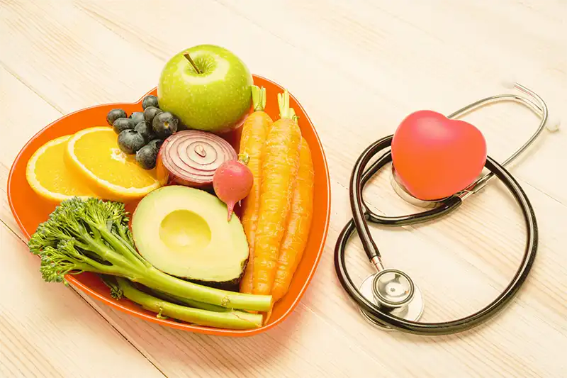 Heart shaped plate with healthy fruits veggies on table next to stethoscope for heart failure therapy
